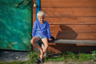 köyde evin yanında bir bankta oturmuş çizgili tişört içinde küçük bir çocuk