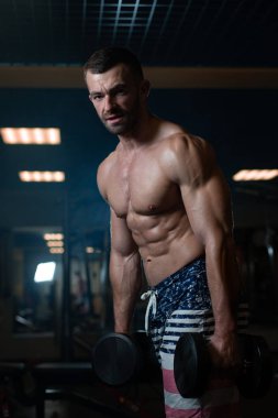 Güzel genç kaslı adam dumbbells ile el spor salonunda poz