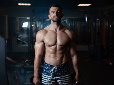 Güzel genç kaslı adam dumbbells ile el spor salonunda poz