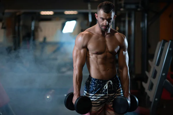 Güzel genç kaslı adam dumbbells ile el spor salonunda poz
