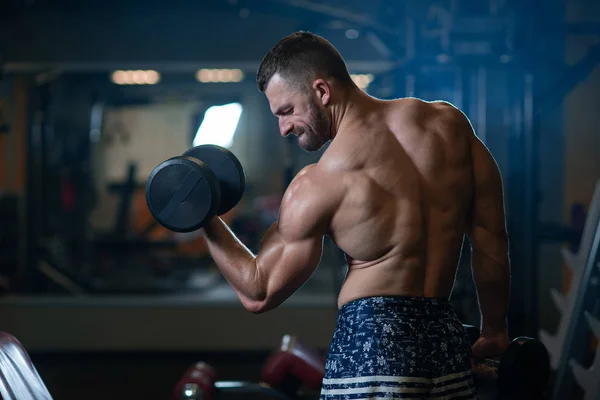 Handsome young muscular man exercising with dumbbells. Guy trains his bicep