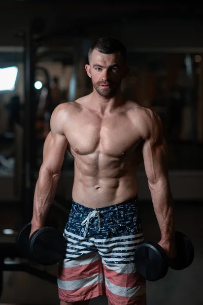 Güzel genç kaslı adam dumbbells ile el spor salonunda poz