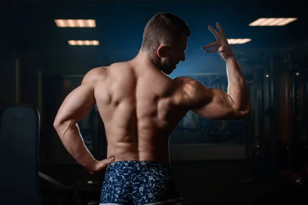 一个肌肉发达的野蛮人在健身房里摆姿势 露出他的二头肌和背部 健康生活方式的概念 — 图库照片