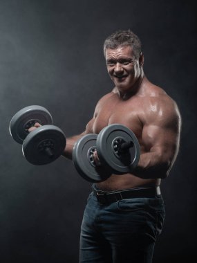 Güçlü kas adam trenler duman siyah arka plan üzerine dumbbells ile