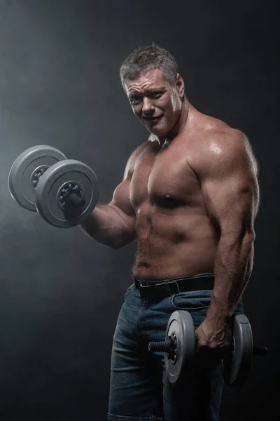 Potente Hombre Musculoso Entrena Con Mancuernas Sobre Fondo Negro Humo — Foto de Stock