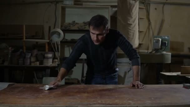 Homem em uma loja de carpinteiros limpa a mesa de serragem — Vídeo de Stock
