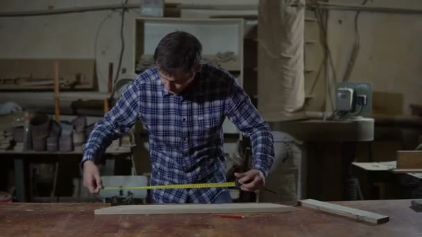 Trabajador en camisa de trabajo mide tablero de madera con regla amarilla larga en un banco de trabajo — Vídeo de stock
