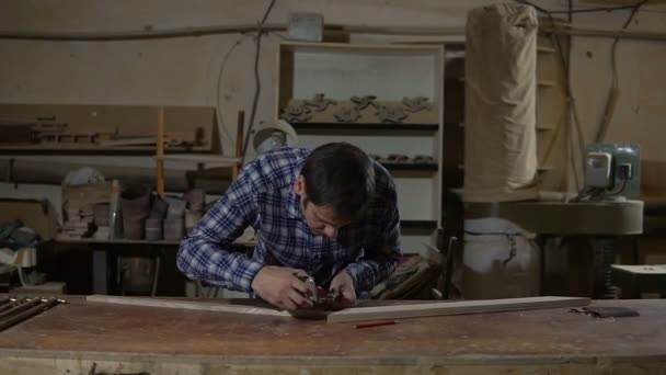 O trabalhador na camisa de trabalho mede a placa de madeira com régua amarela longa em uma bancada — Vídeo de Stock