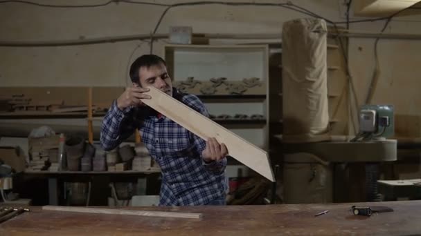 O trabalhador na camisa de trabalho mede a placa de madeira com régua amarela longa em uma bancada — Vídeo de Stock