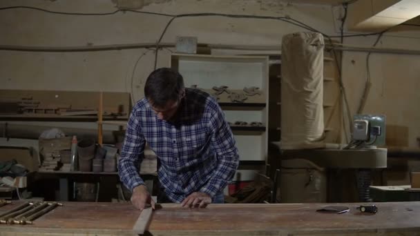 Worker in work shirt measures wooden board with long yellow ruler on a workbench — Stock Video