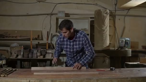 Carpintero pule la tabla de madera con papel de lija en el escritorio. Trabajo en el taller de carpintería — Vídeos de Stock