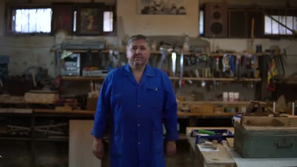 Mature carpenter approaches the camera and stands in a confident pose in his workshop — Stock Video