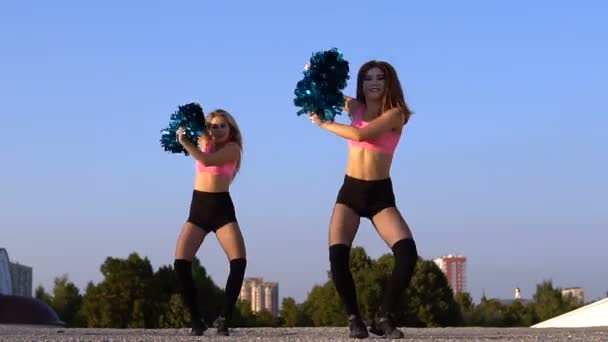 Two girls cheerleaders with pompons dancing outdoors — Stock Video