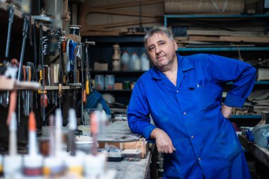 Olgun bir marangoz kamera yaklaşımlar ve atölyesini emin poz duruyor