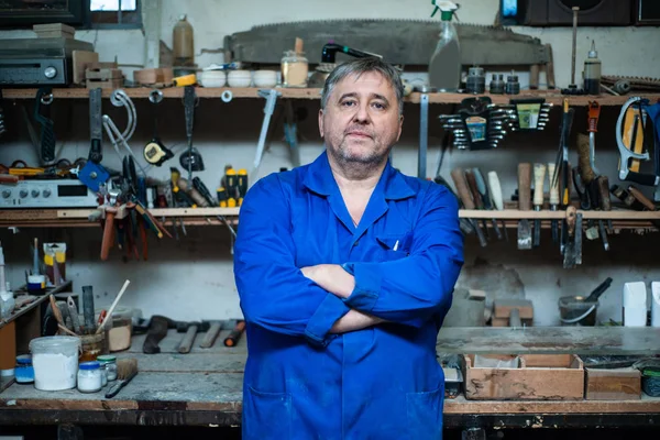 A Mature carpenter approaches the camera and stands in a confident pose in his workshop