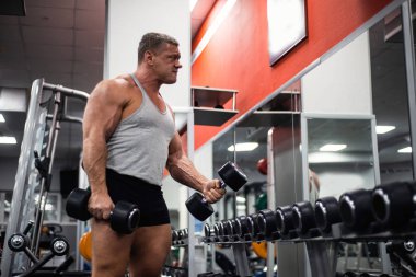 Spor salonunda büyük atletik adam trenler. Eğitim pazı bir dumbbells ile