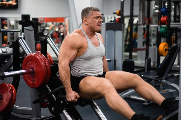 Big muscular man trains his legs in the gym. Health and fitness concept