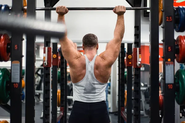 Big muscular man trains his shoulders with a barbell in the gym. Health and fitness concept