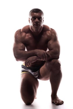 Studio dizlerinin üzerinde oturan beyaz arka plan üzerinde gömleği kasların gösterilen büyük güçlü bir adam