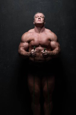 Büyük güçlü bir adam gömleksiz bir stüdyoda bir grunge siyah duvara kasları trenler