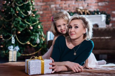 Anne ve kızı bir Noel ağacı arka planda hediye kutuları ile yerde yatarken