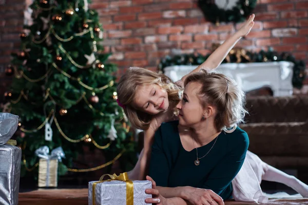 Mom and daughter having fun on the floor with gift boxes on the Christmas tree background