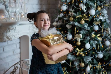 Mutlu kız eğleniyor ve şömine ve Noel ağacı yakınındaki bir hediye sarılarak