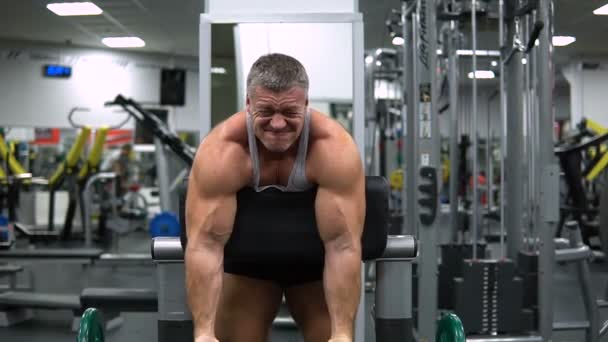 Hombre entrena bíceps con una barra en el gimnasio — Vídeos de Stock