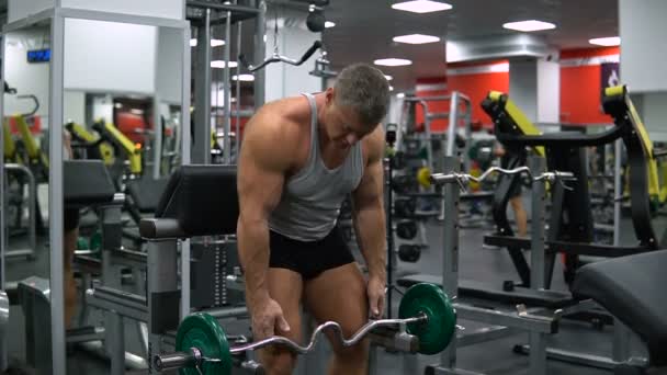 Hombre entrena bíceps con una barra en el gimnasio — Vídeo de stock