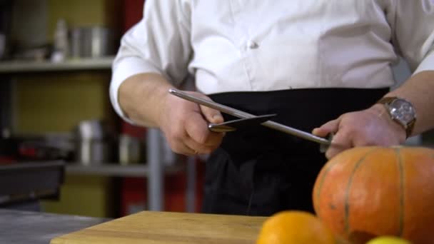 Шеф-повар точит нож на коммерческой кухне для приготовления тыквы — стоковое видео