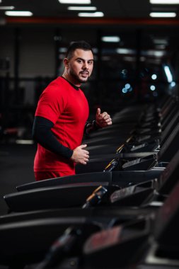 Genç adam kırmızı elbiseler spor salonunda koşu bandı üzerinde çalışan spor giyim