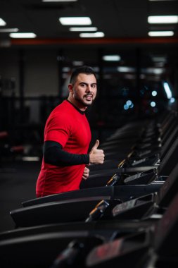 Genç adam kırmızı elbiseler spor salonunda koşu bandı üzerinde çalışan spor giyim