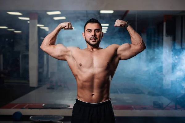 Poz, kasları spor salonunda kapalı gösteren güzel atletik erkek