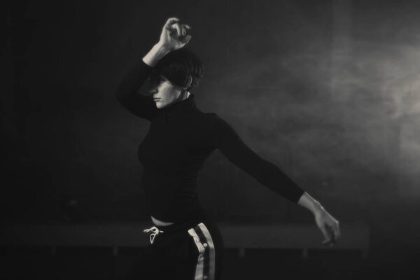 modern young beautiful dancer in black clothes posing against the Studio in the smoke