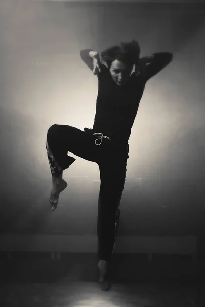 modern young beautiful dancer in black clothes posing against the Studio in the smoke