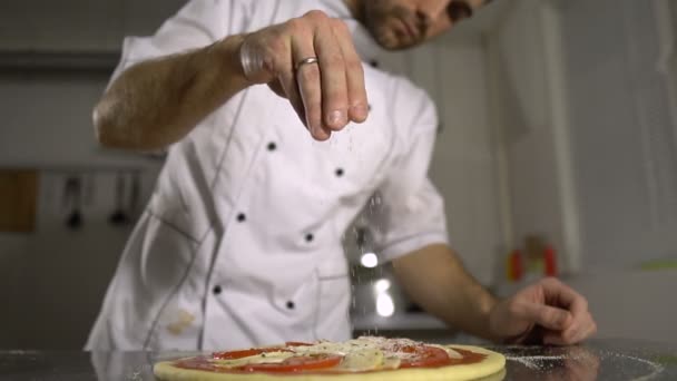 Шеф-повар посыпал специи на готовую пиццу на кухне — стоковое видео