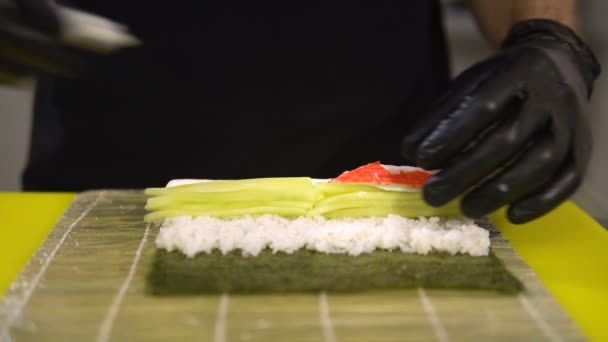 As mãos do cozinheiro preparam pratos japoneses, o cozinheiro faz o sushi, prepara o rolo de sushi, põe um recheio muito saboroso — Vídeo de Stock