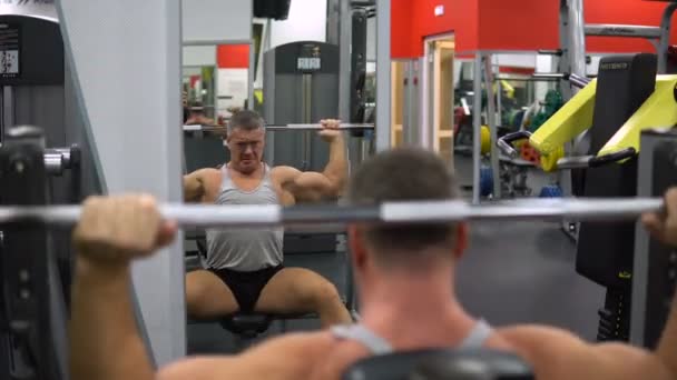RÚSSIA, TOGLIATTI - SETEMBRO 20, 2018: O homem musculoso treina os ombros com uma barra no ginásio. Conceito de saúde e fitness — Vídeo de Stock