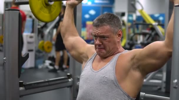 Russland, Togliatti - 20. September 2018: In der Sporthalle trainiert ein muskulöser Mann seine Schultern mit einer Langhantel. Gesundheits- und Fitnesskonzept — Stockvideo