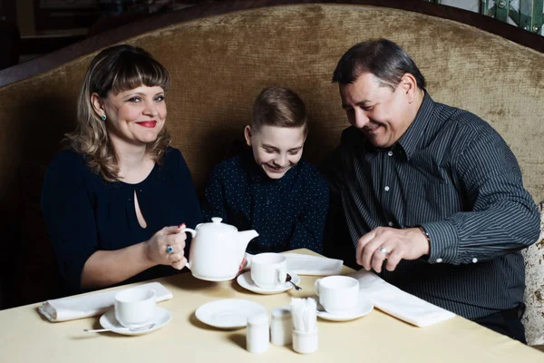 Family came together in a cafe. Mom, dad, little son drink tea. They are happy together. Happy family lunch concept.