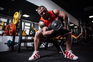 Rusya, Samara - 18 Aralık 2018: spor salonunda eğitim iri atletik bir adam. Pazı bir bankta oturan dumbbells ile eğitim