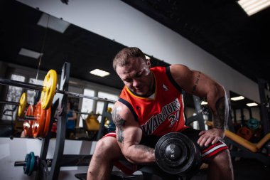 Rusya, Samara - 18 Aralık 2018: spor salonunda eğitim iri atletik bir adam. Pazı bir bankta oturan dumbbells ile eğitim