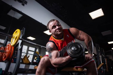 Rusya, Samara - 18 Aralık 2018: spor salonunda eğitim iri atletik bir adam. Pazı bir bankta oturan dumbbells ile eğitim