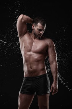 Gömleksiz yakışıklı genç adam su ile poz yüz ve göğüs Studio çekimde su sıçramalarına
