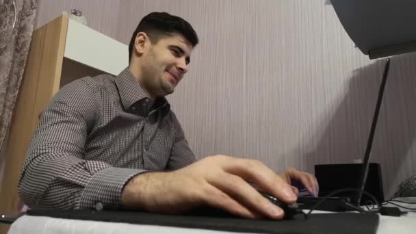 Молодий чоловік працює на ноутбуці і сміється над тим, що він бачив на екрані комп'ютера — стокове відео