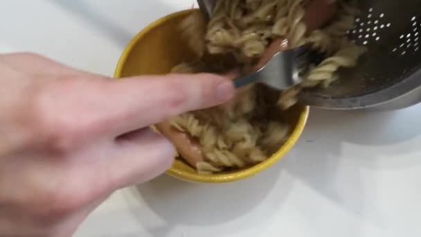 Hands putting on pasta with sausages in a bowl with a fork. Cooking delicious food — Stock Video