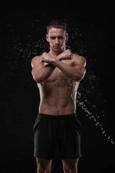 Wet young man crossed his fists, standing in a belligerent pose with water splashes