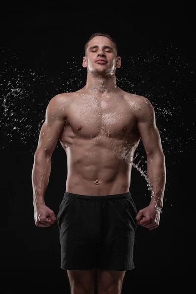 Schöner junger Mann posiert in Studioaufnahme mit Wasserspritzern auf Gesicht und Brust — Stockfoto
