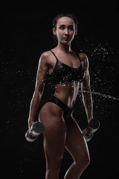 Красива дівчина тренується з гантелями з водяними бризками на обличчі і грудях в студії постріл — стокове фото