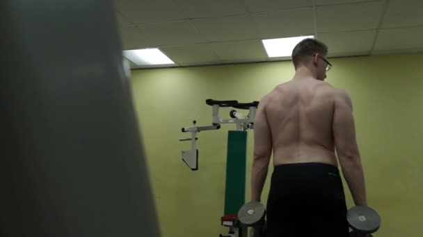 Jeune homme entraîne ses épaules avec des haltères dans la salle de gym — Video